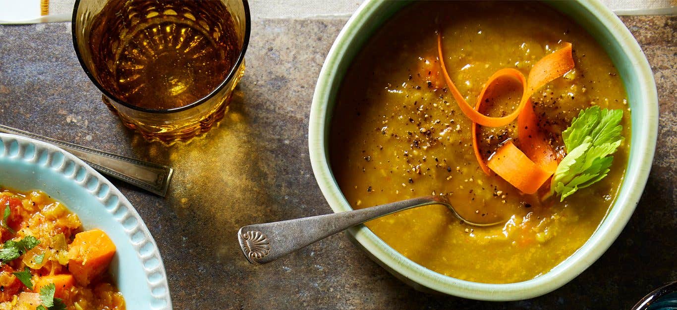 Slow-Cooker Split Pea Soup garnished with a carrot ribbon and celery leaves in a light blue bowl