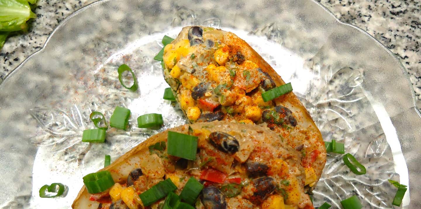 Two Southwestern Vegan Twice Baked Potatoes on a glass plate, garnished with green onion