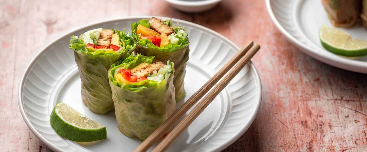 Spicy Tempeh Mango Spring Roll, cut in half, on a plate with chopsticks and a wedge of lime