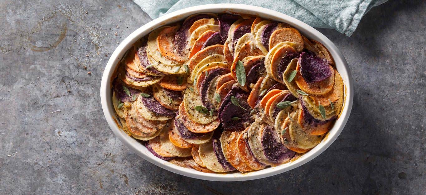 Vegan Sweet Potato Gratin with fresh sage leaves in a white casserole dish