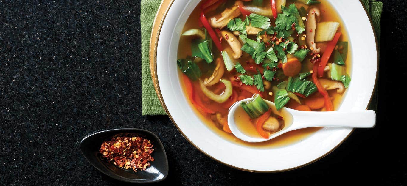 Sweet and Sour Vegetable Soup in a white bowl with a soup spoon on a black granite countertop