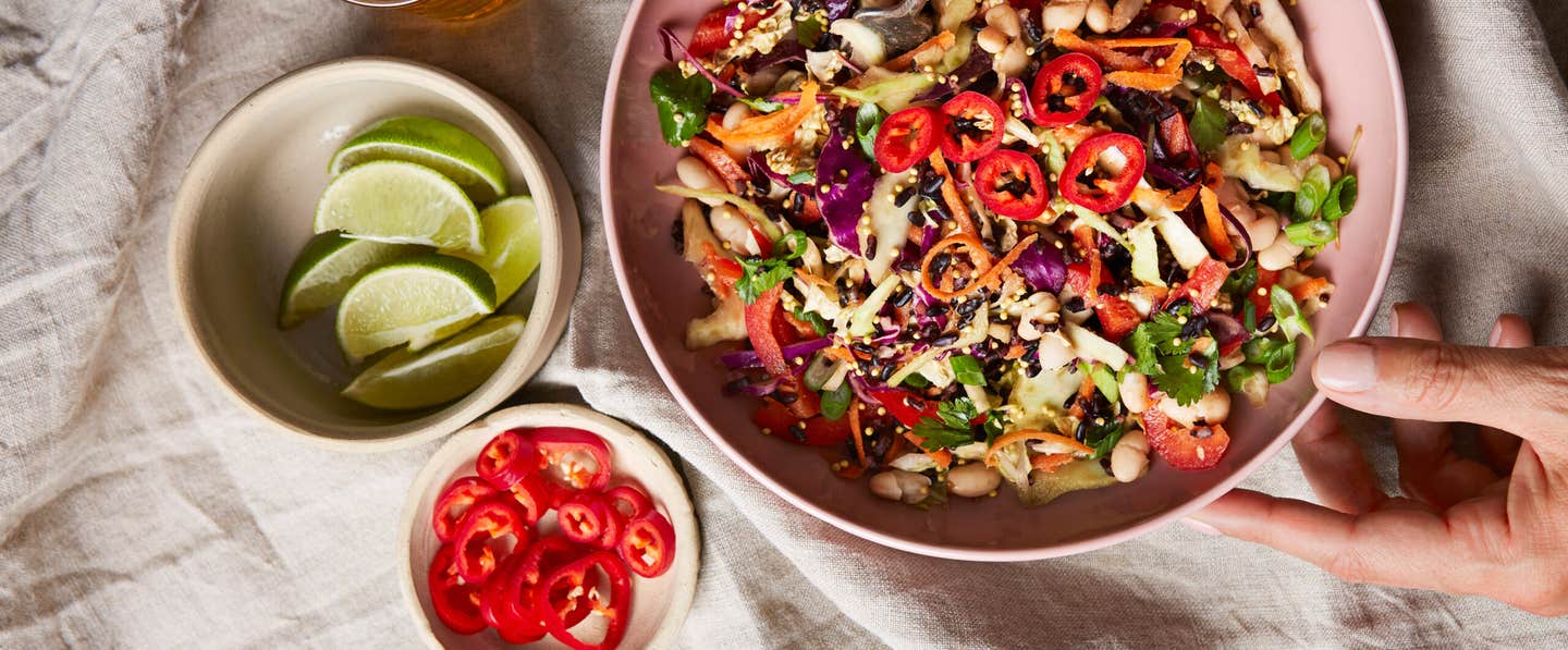 Szechwan Coleslaw in a pink ceramic bowl with a woman's hand touching the right side