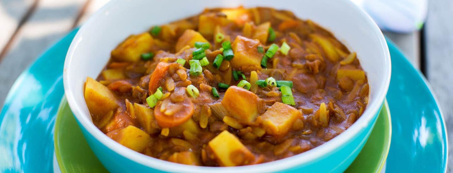 A blue bowl on a green plate filled with Curried Tomato Lentil Soup (Shorba Addis)