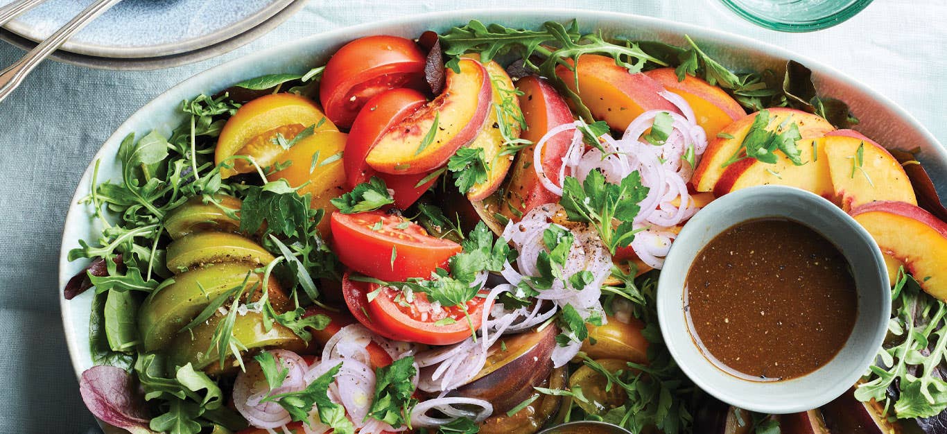 each and Tomato Salad on a light blue serving platter with a small bowl of vinaigrette