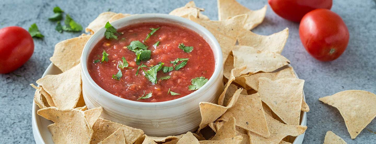 Roasted Tomato Salsa with baked chips next to fresh tomatoes and a few cilantro leaves