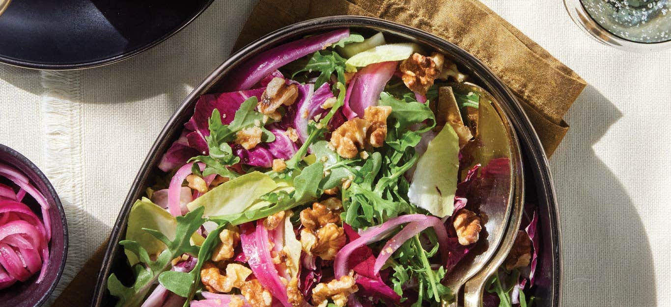 Tricolor Salad with Quick-Pickled Onions on an oval serving platter with gold metal serving spoons