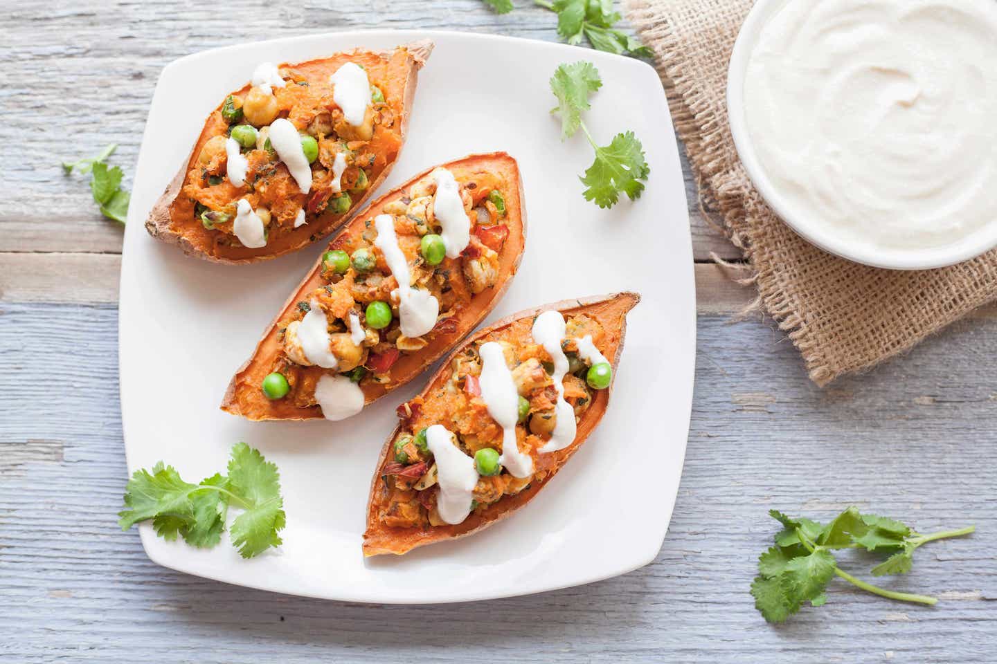 Twice-Baked Sweet Potatoes on a white plate, next to a bowl of vegan sour cream with cilantro dotted around