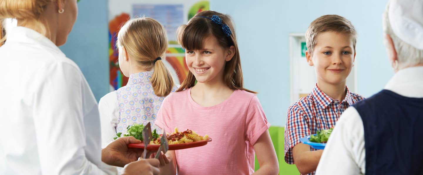 Smiling elementary children receive a healthy plant-based school lunch