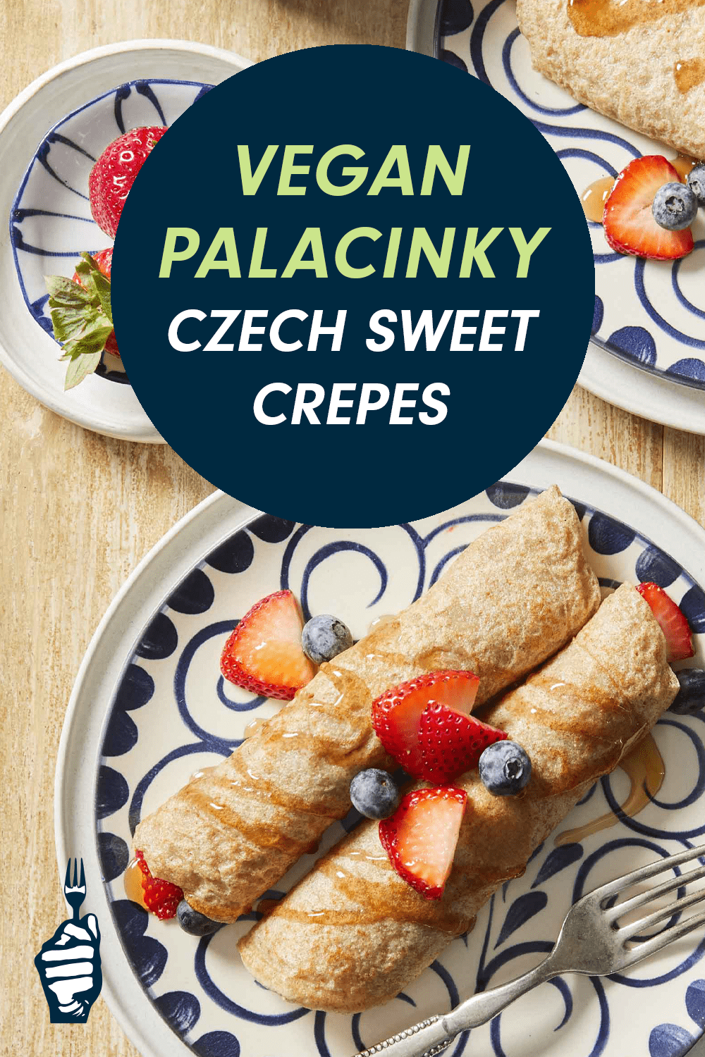 A plate of crepes, rolled and garnished with fresh berries and a drizzle of maple syrup. A circular badge over the top of the image reads, "Vegan Palacinky (Czech Sweet Crepes)"