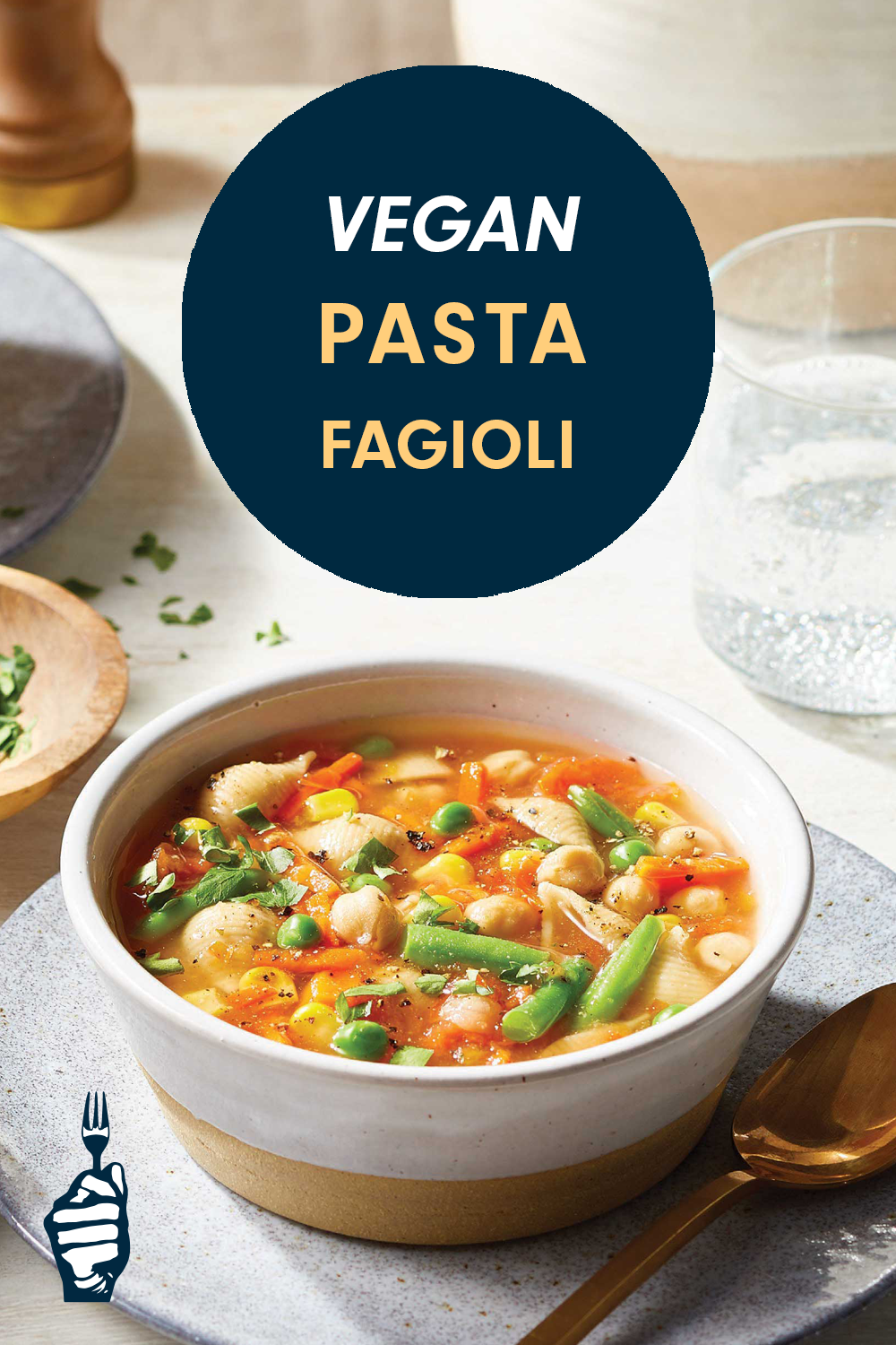 A rustic ceramic bowl of soupy-looking pasta with beans, peas, carrots and other veggies, next to a spoon and glass of water. Text reads, "Vegan Pasta Fagioli"