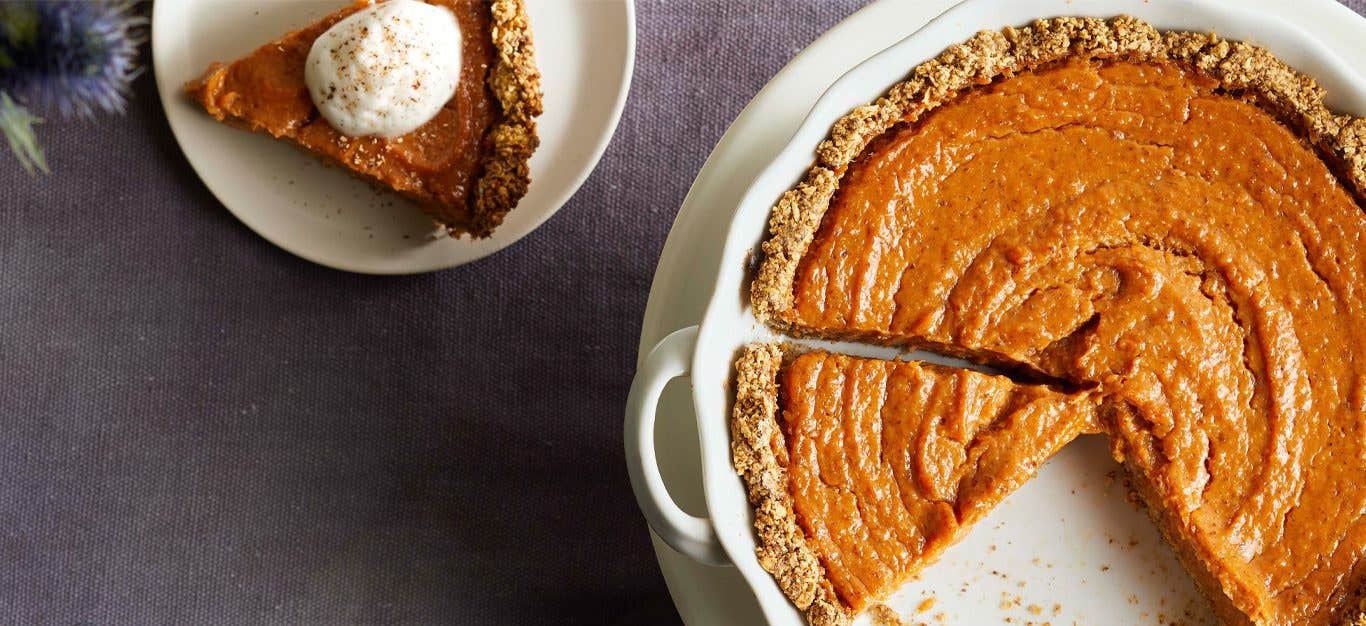 Vegan Sweet Potato Pie in a white pie tin with a slice topped with whipped cream sitting next to it on a saucer