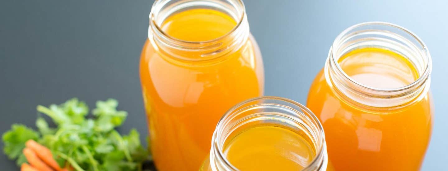 Three mason jars of orange-hued vegetable stock against a grey background