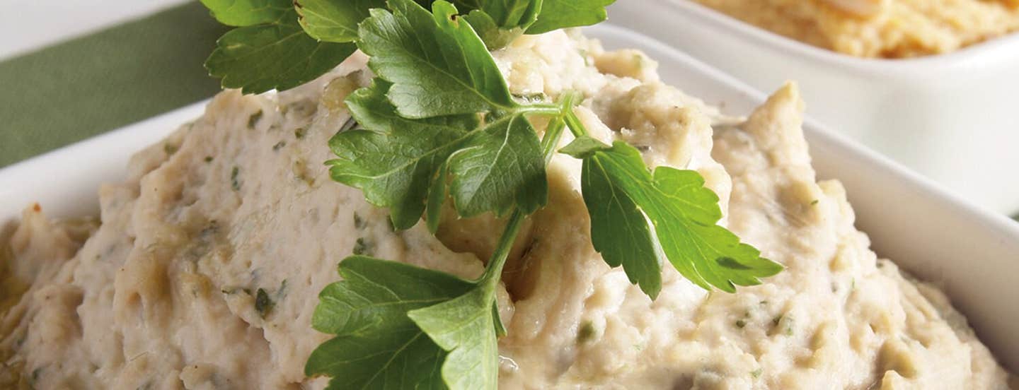 White Bean Hummus with Fresh Thyme and Basil in a white bowl with a sprig of flat-leaf parsley on top