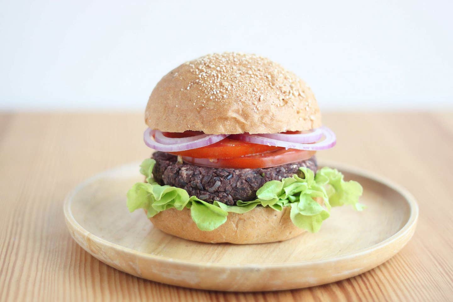 One veggie burger, with lettuce, a veggie pattie, and tomato and red onion slices on a whole grain bun. On a wooden plate