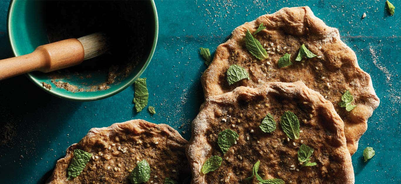 Za’atar-Spiced Flatbreads (Manakeesh) on a blue tabletop next to a bowl za'atar spice