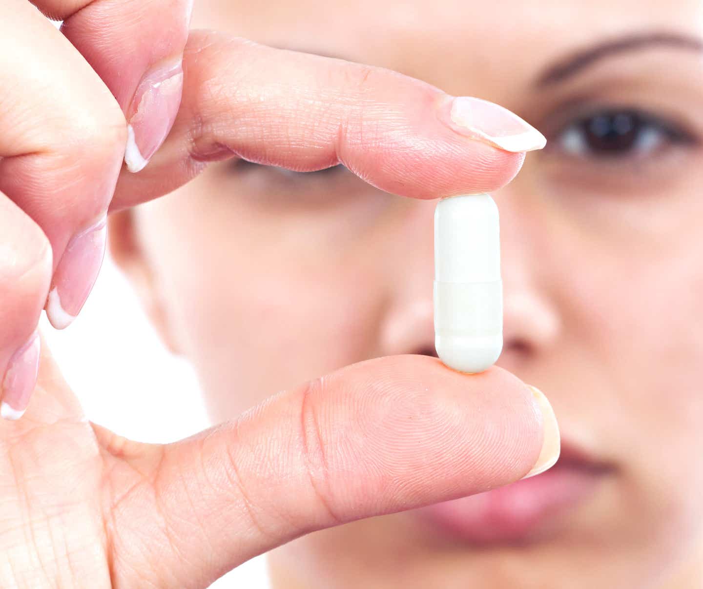 Close-up of unidentified woman holding a white capsule in front of her face