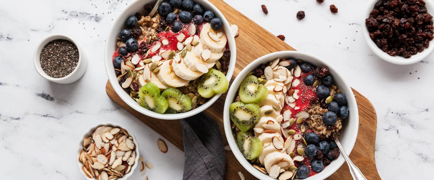 Two bowls of Berry-Licious Overnight Oatmeal next to smaller bowls of raisins, slivered almonds, and chia seeds