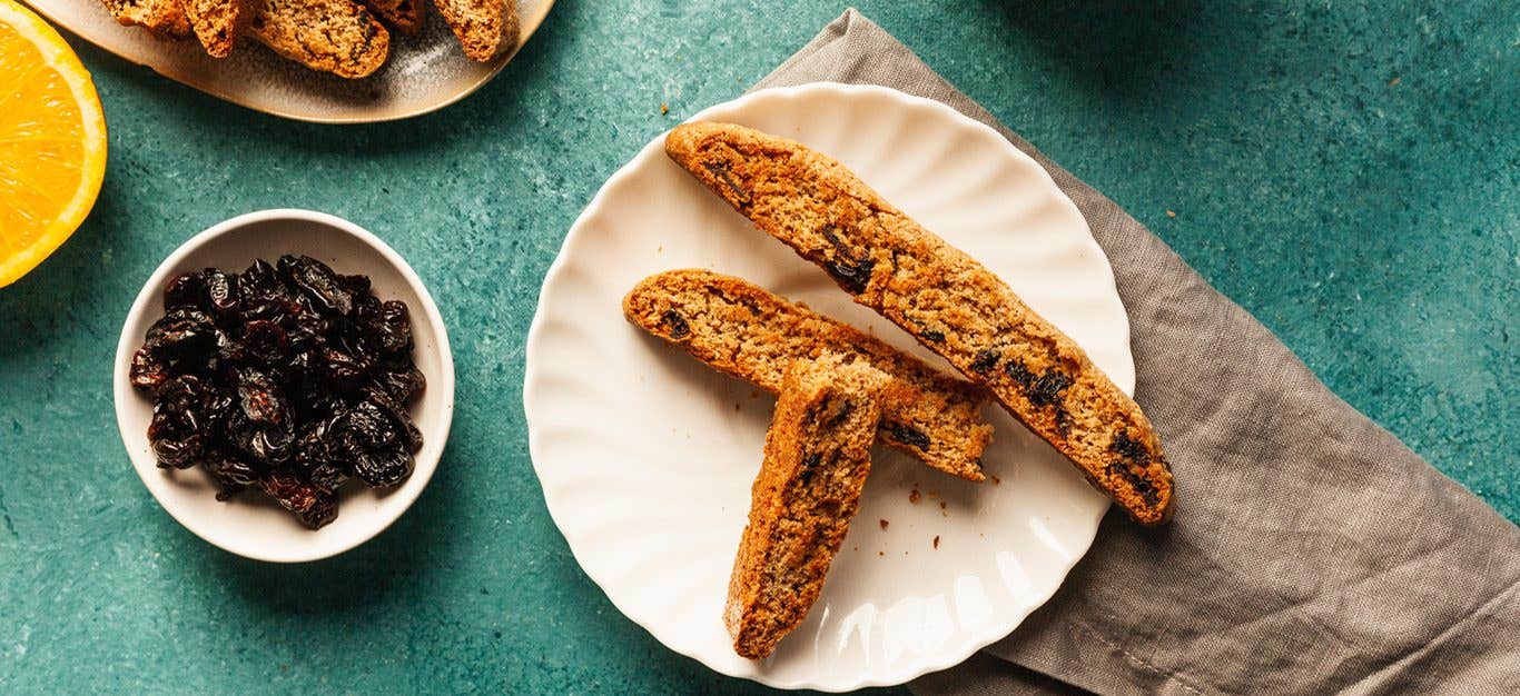 Three slices of Cranberry-Orange Biscotti on a white plate next to a small bowl of dried cranberries