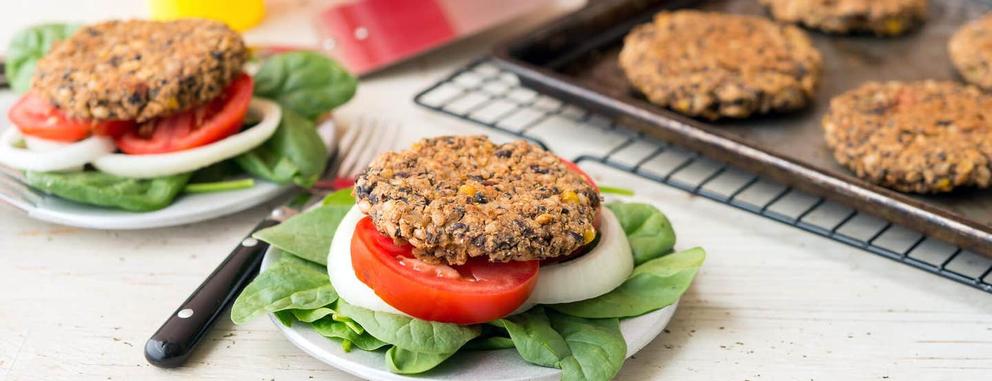 A black bean burger on a plate with fresh greens, a slice of tomato, and a slice of onion