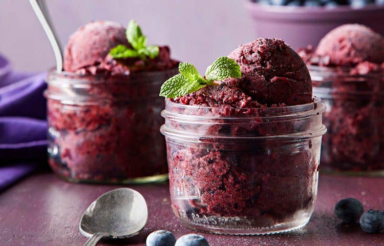 Deep purple blueberry and mint nice cream shown from the side in a clear glass Mason jar, topped with sprigs of mint - vegan ice cream recipe