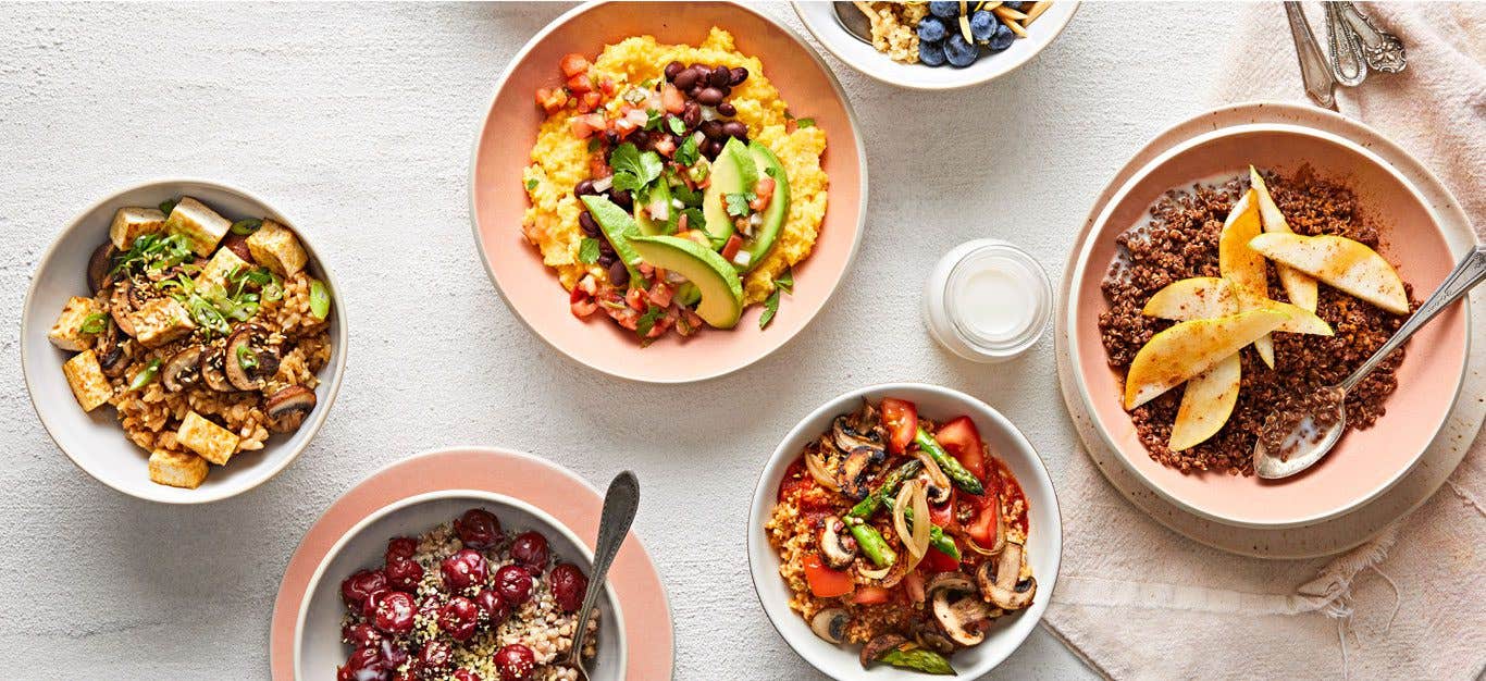 A top-down shot of a white tablecloth topped with six colorful vegan breakfast bowls