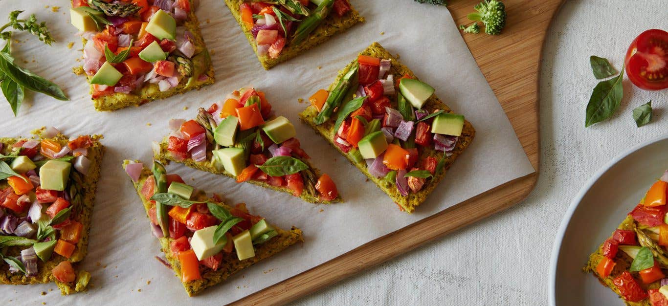 square-cut pizza loaded with veggies including asparagus, tomato, and avocado, with a mildly green crust made of broccoli