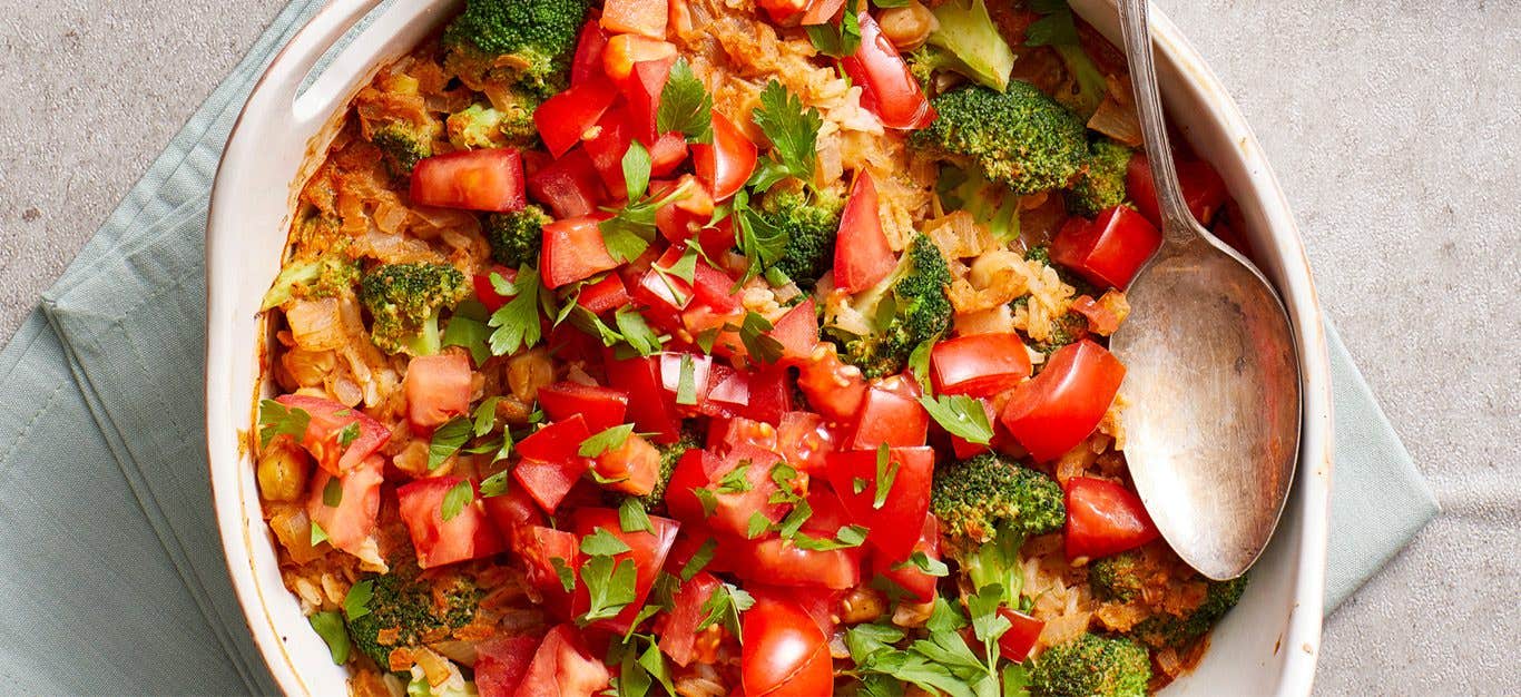 brown rice casserole with broccoli and tomatoes, shown in a round white casserole dish