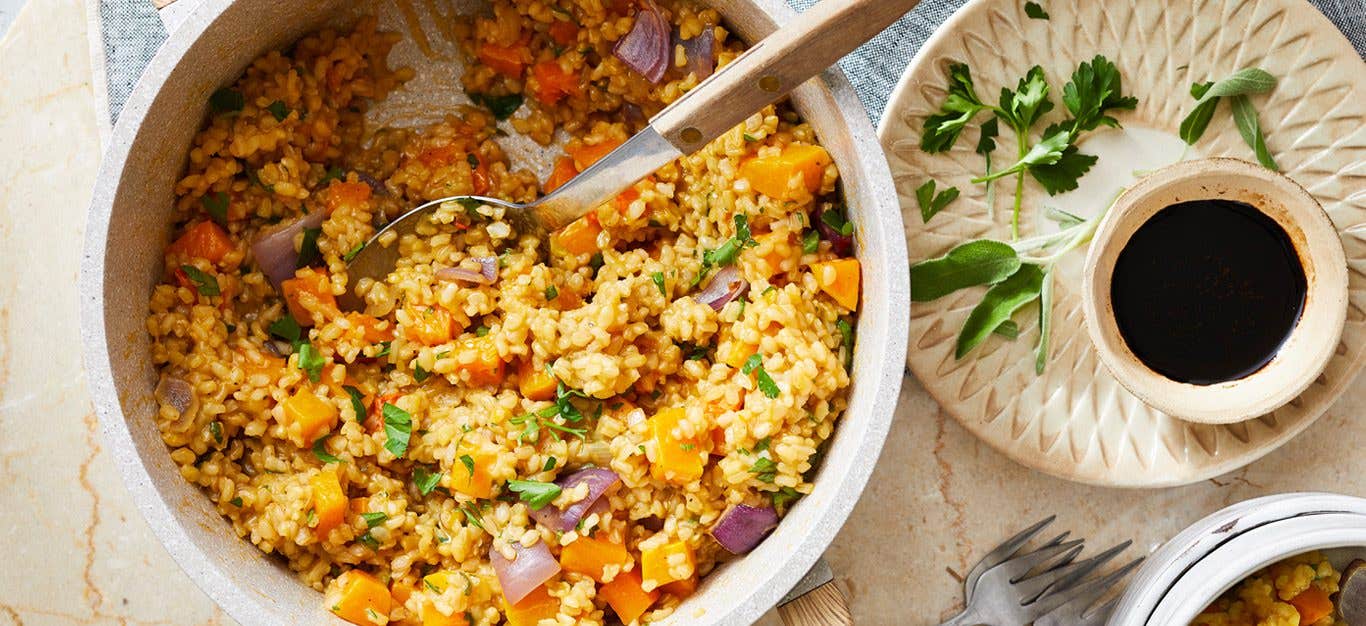 Butternut squash risotto in a pot with balsamic glaze in a cup to the side