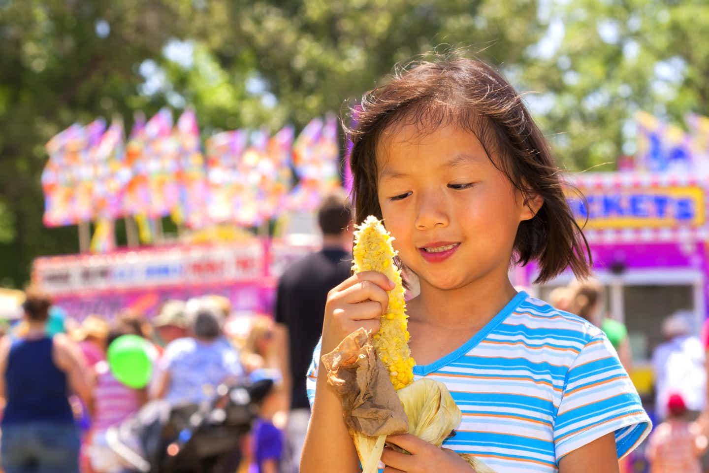 A young girl at a carnival eating an ear of corn