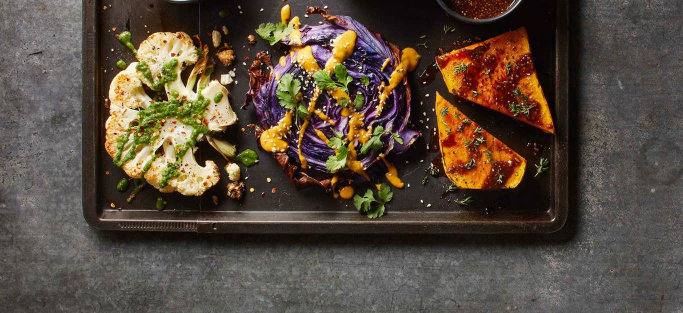 Three slices of grilled veggie steaks, one cauliflower, one cabbage, one cauliflower, drizzled with sauce