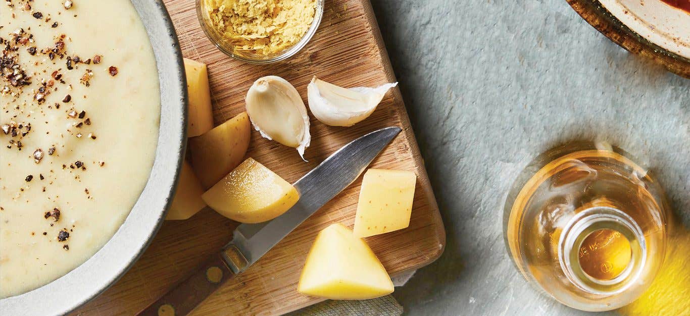 Vegan potato cheese sauce in a bowl surrounded by chunks of potato and garlic cloves