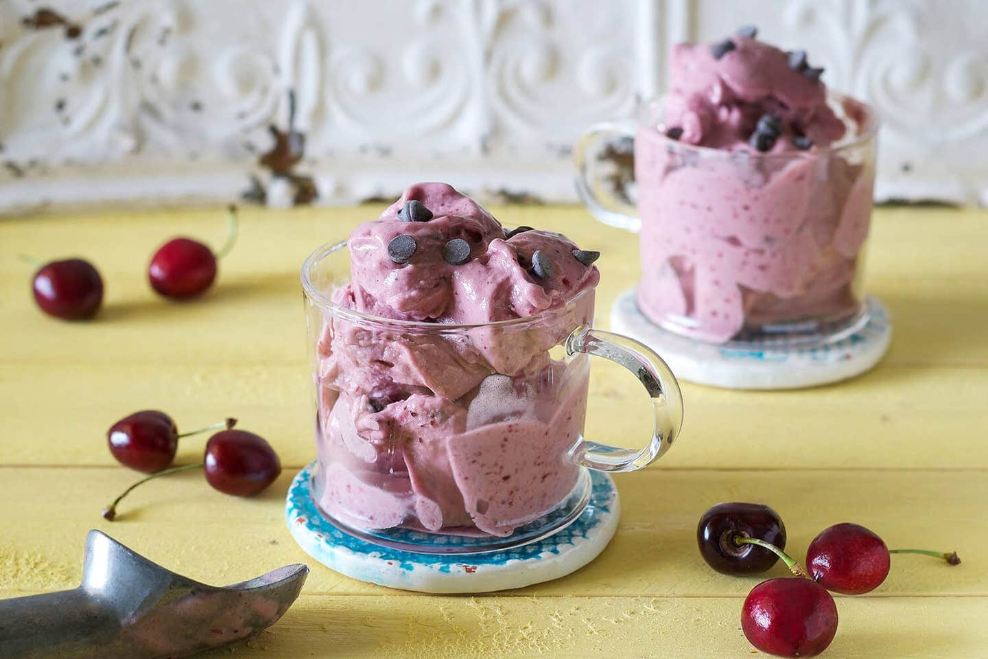 Two glass mugs of Cherry Soft-Serve Ice Cream with fresh cherries strewn on the table