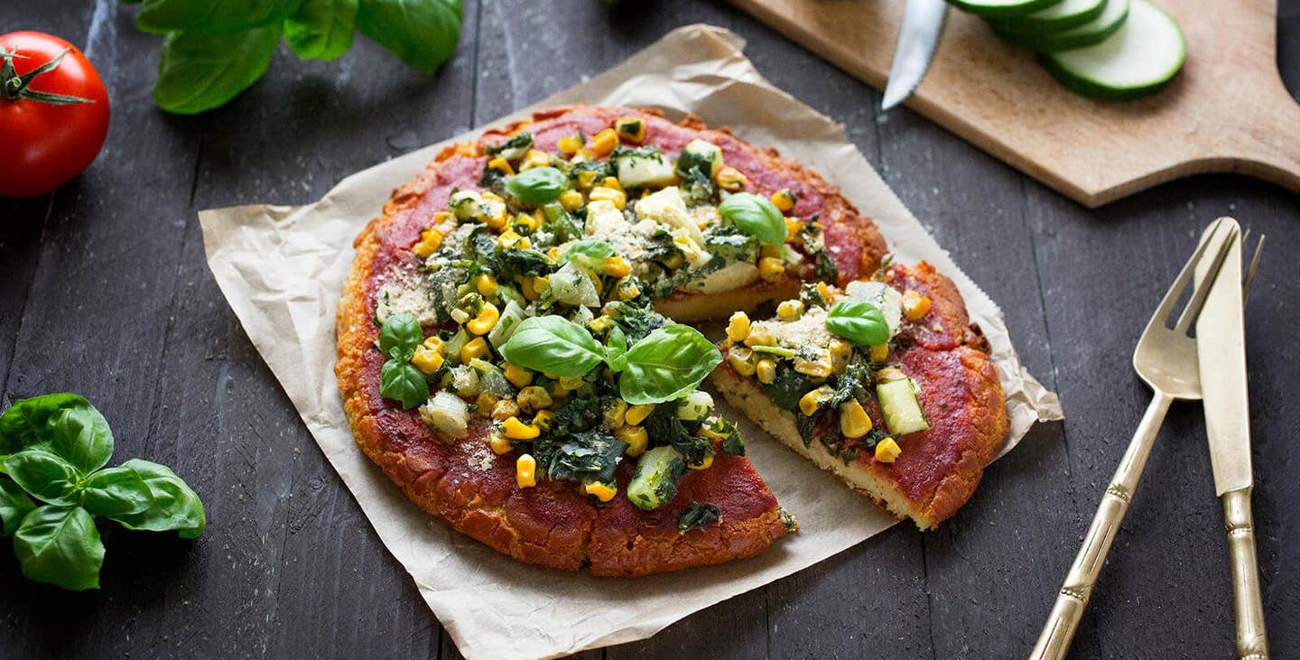 Chickpea Flour Pizza Crust (Gluten-Free) on parchment paper on a wooden table top with fresh basil and tomato to the side