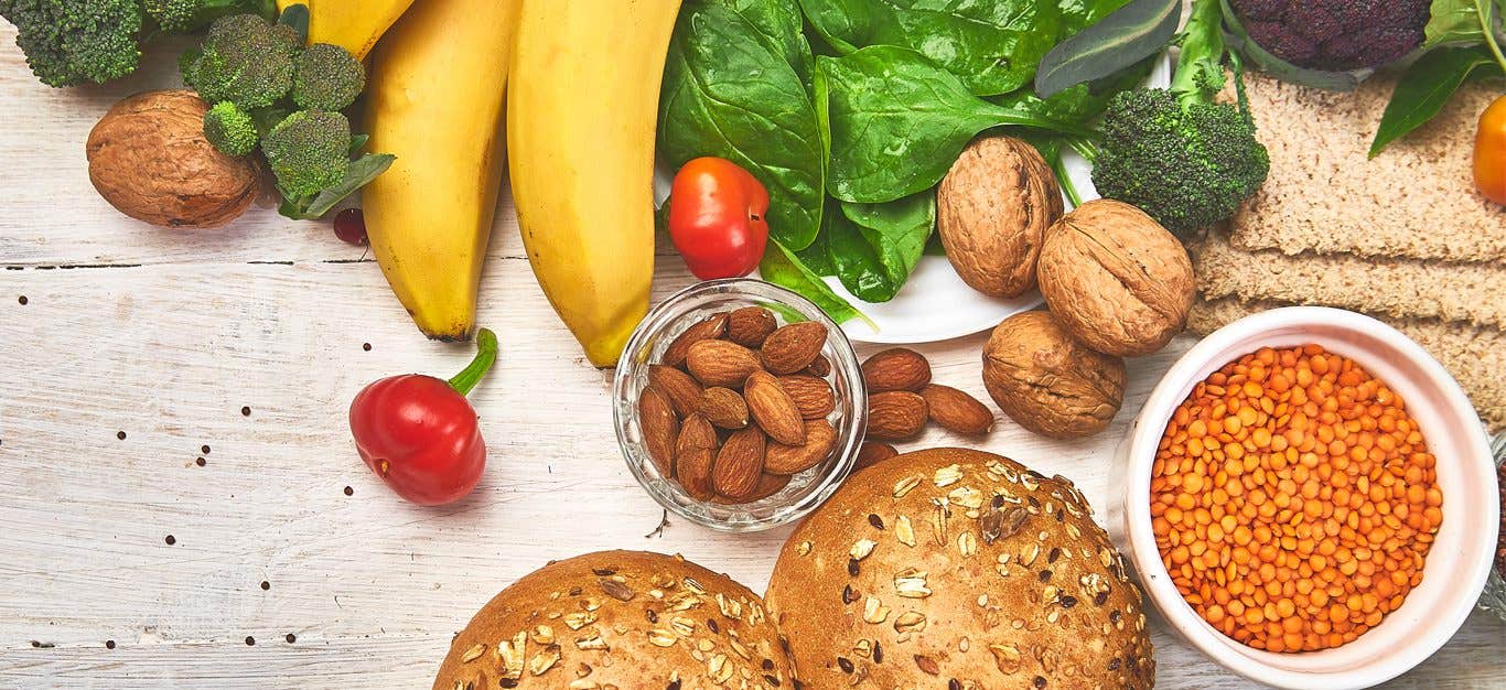 Vegetables, fruit, nuts, lentils and bread lay spread out on a white counter