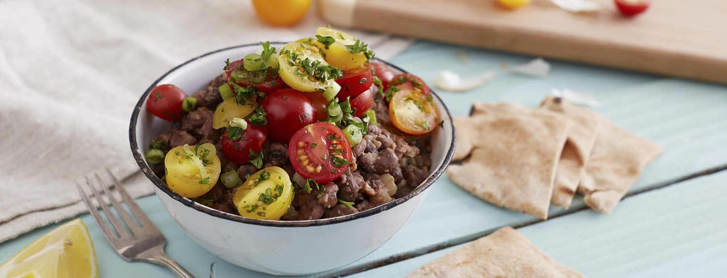 Egyptian Breakfast Beans (Ful Medames) garnished with fresh herbs with pita squares and a wedge of lemon