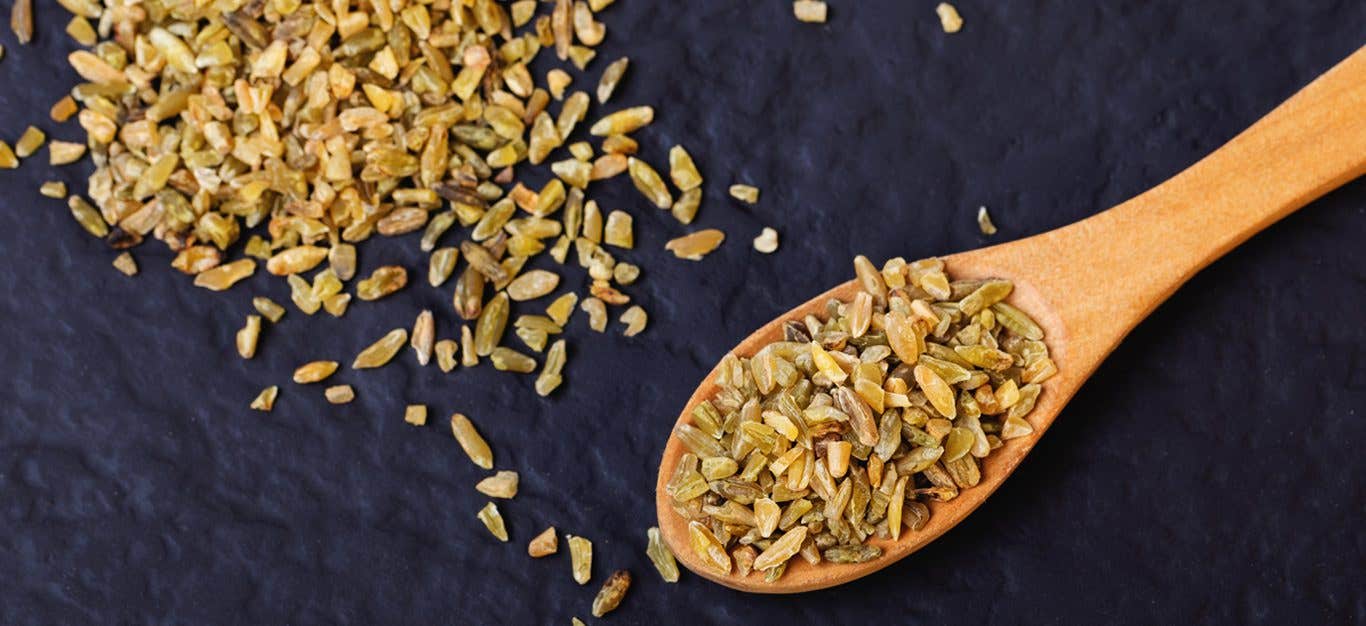 Freekeh grains in a wooden spoon and scattered across a black table