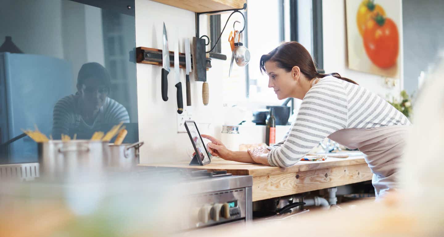 A woman in a modern kitchen leans over a heavy duty wooden kitchen bench, looking at an eye pad