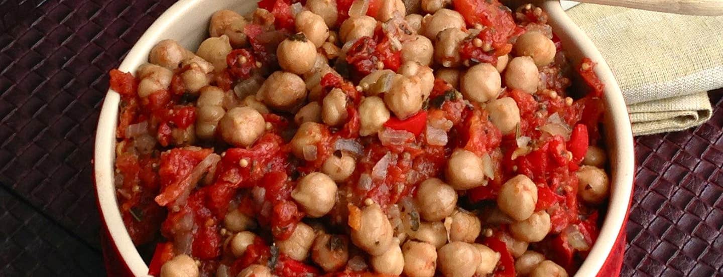 A closeup of Oven-Baked Chickpea Ratatouille in a red bowl with a cloth napkin in the background