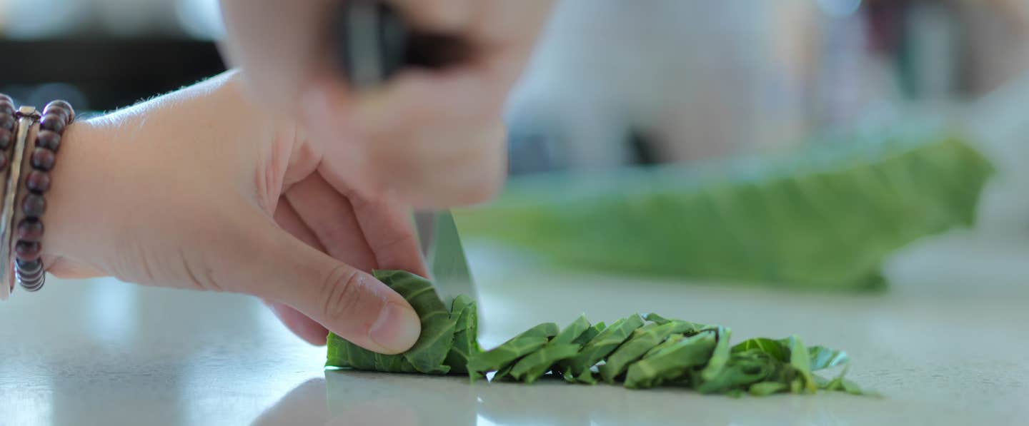 Close up shot of a person cutting rolled collard green thinly