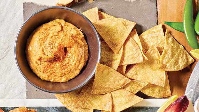 White Bean Queso in a brown ceramic bowl with a side of tortilla chips