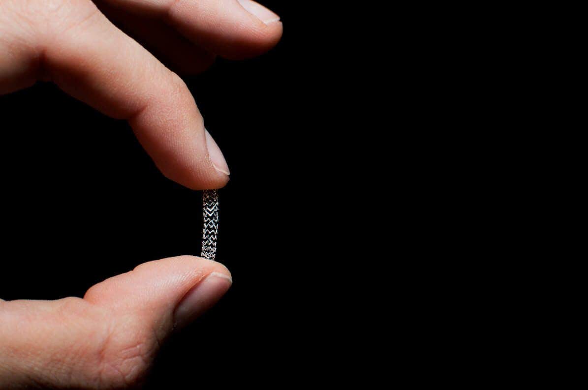 Two fingers holding up a stent, against a black background