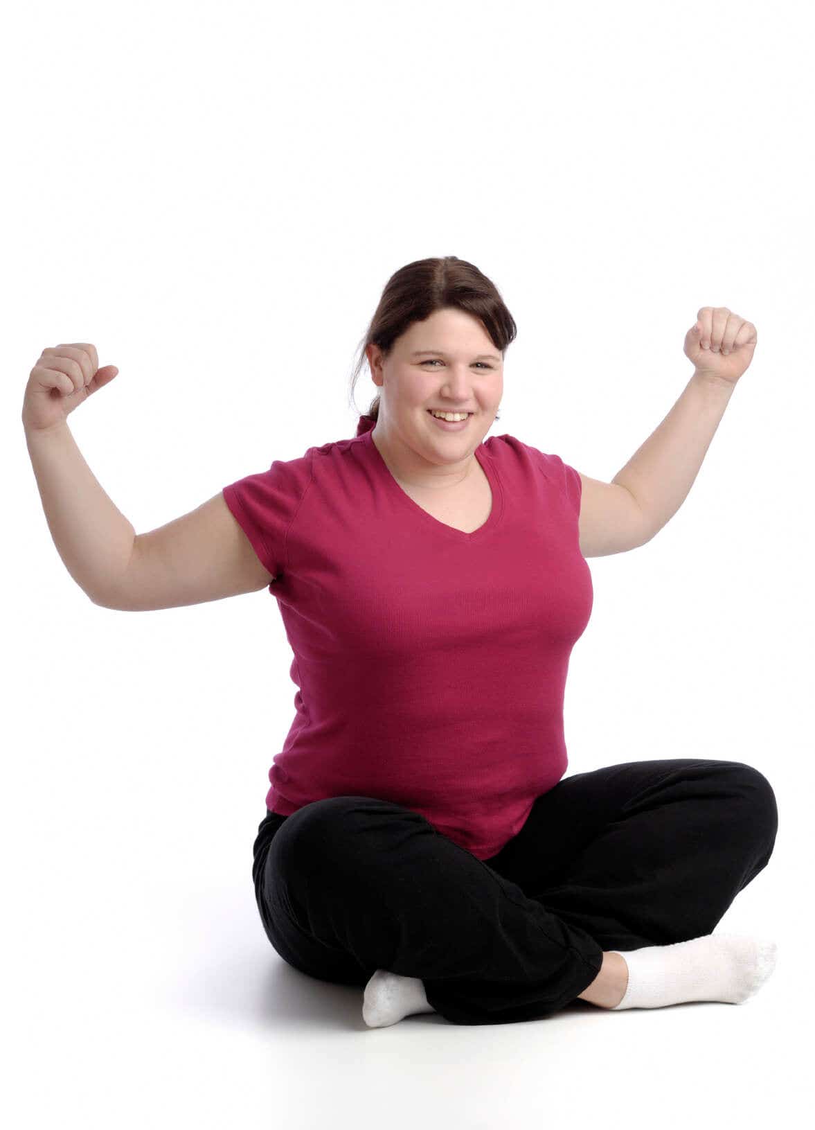 happy overweight young woman sits crosslegged on the floor with her arms lifted out to the side