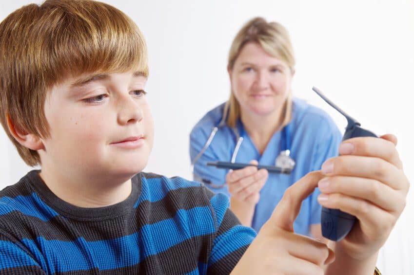 Boy looks at blood glucose monitor with nurse in the background