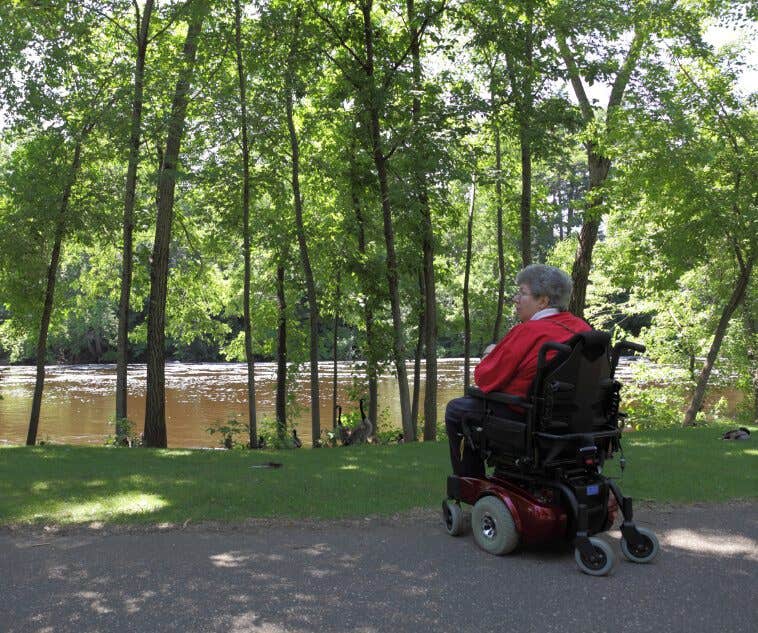 Woman with multiple sclerosis in an electric wheelchair by the bank of a peaceful river