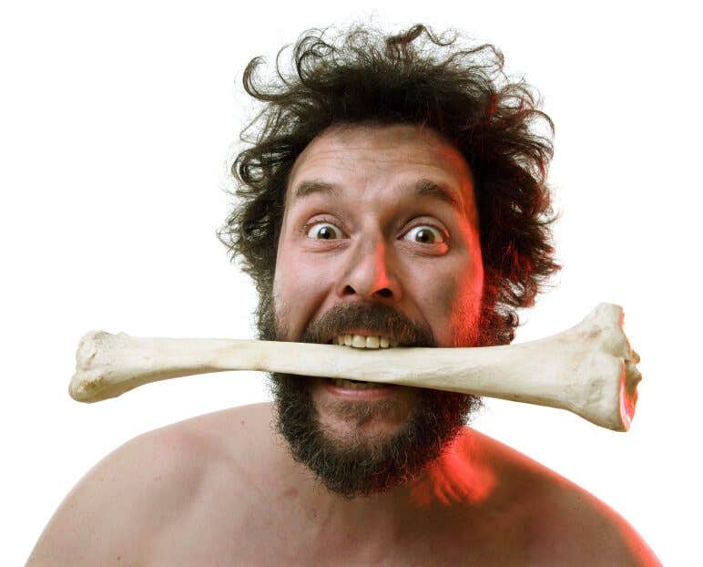 Shirtless, bearded man with a large bone in his mouth