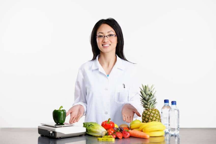 A female doctor in a white lab coat with her hands outstretched in front of her towards a colorful array of fresh fruits and veggies