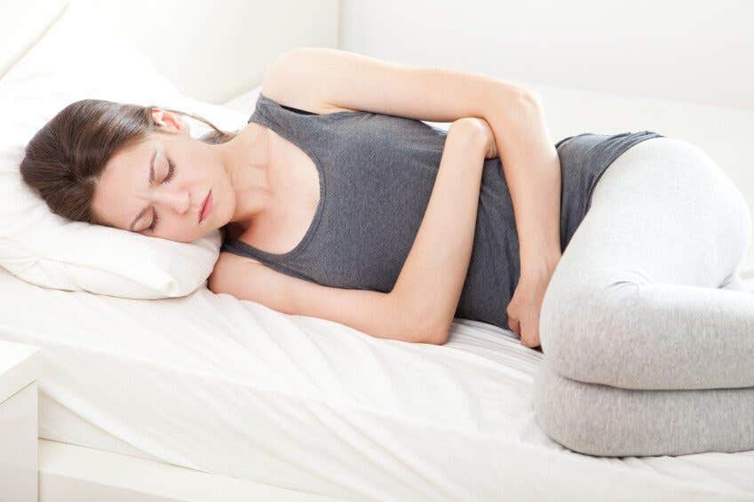 Unhappy young woman in pain lying on bed hands over her stomach