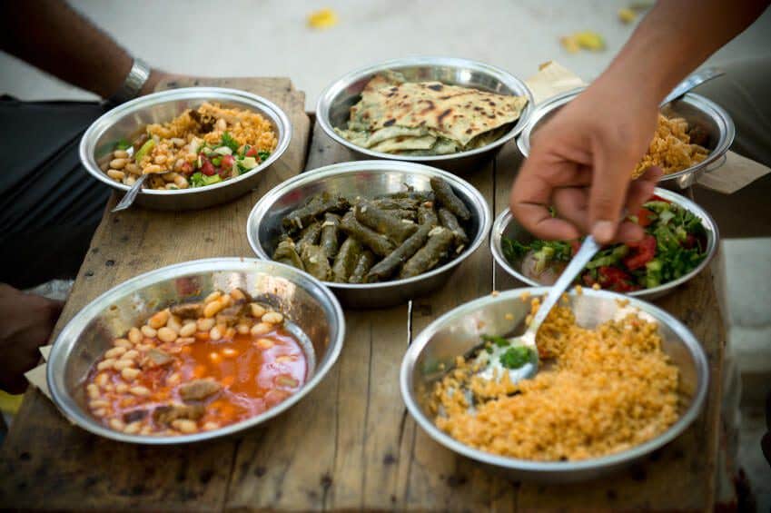 An unidentified man sitting at an outdoor table. On the table are many simple metal bowls will with healthy plant-based dishes