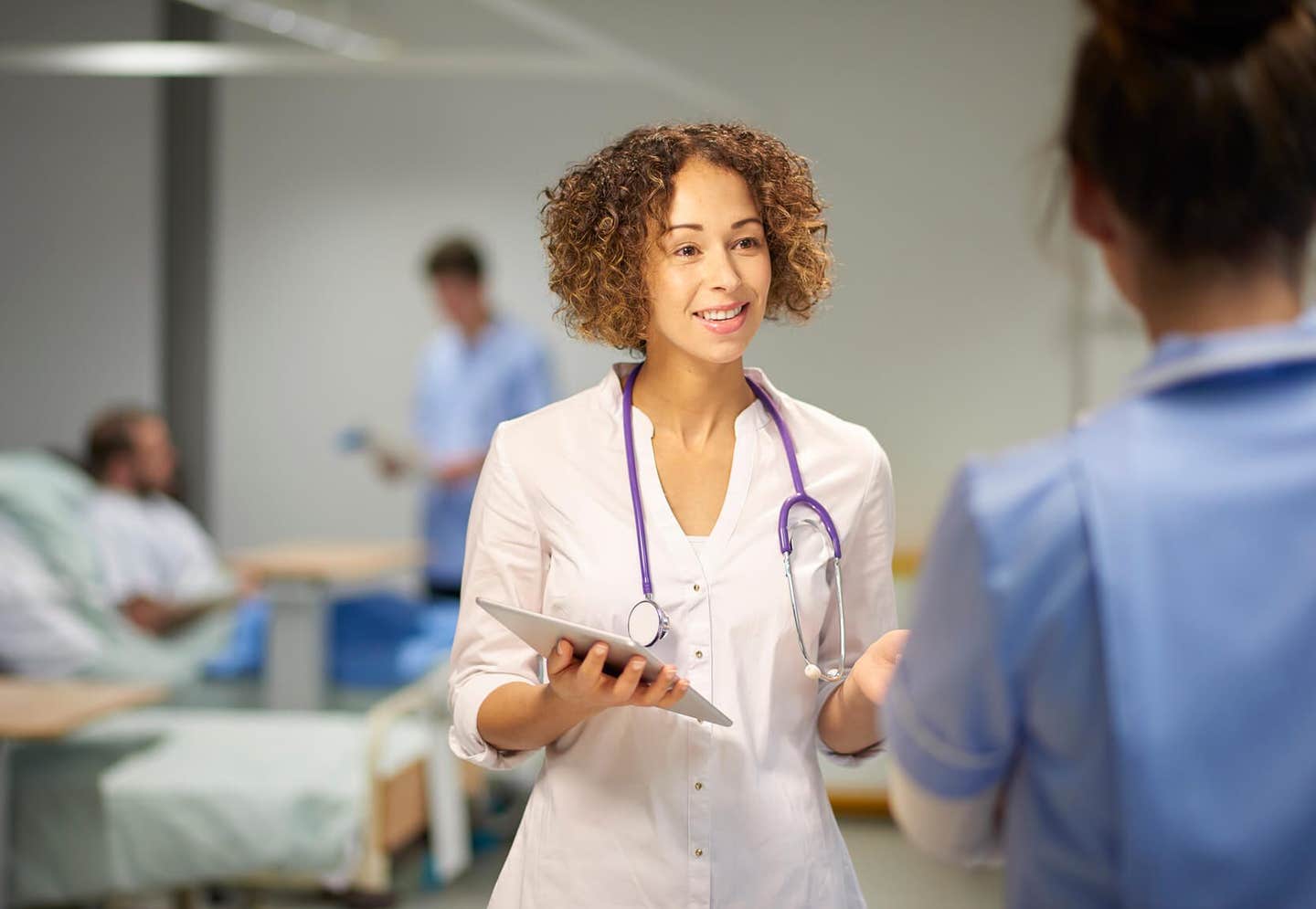 young female doctor with a stethoscope around her neck in a ward, talking to a nurse