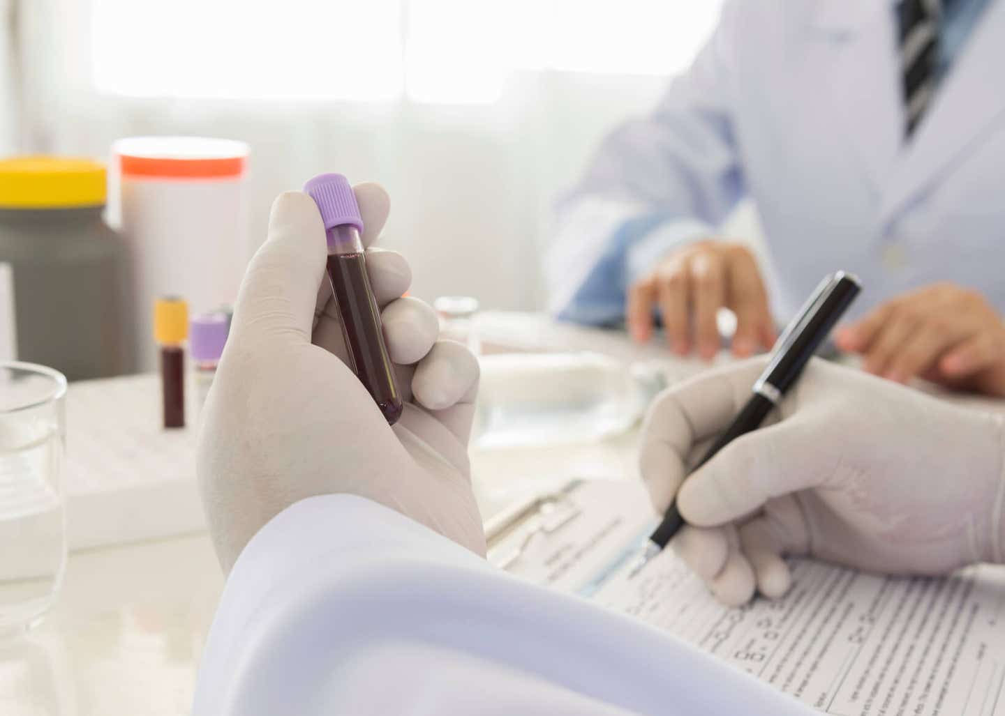 Scene in a lab where lab workers, who are wearing gloves, make notes about vials of blood